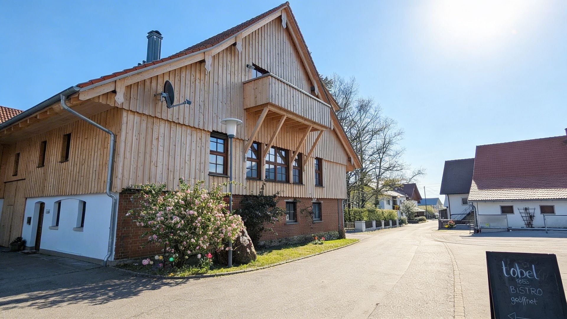 Gutshof tobel1853 im Frühling mit Holzfassade, blühendem Garten und Bistro-Schild im Allgäu