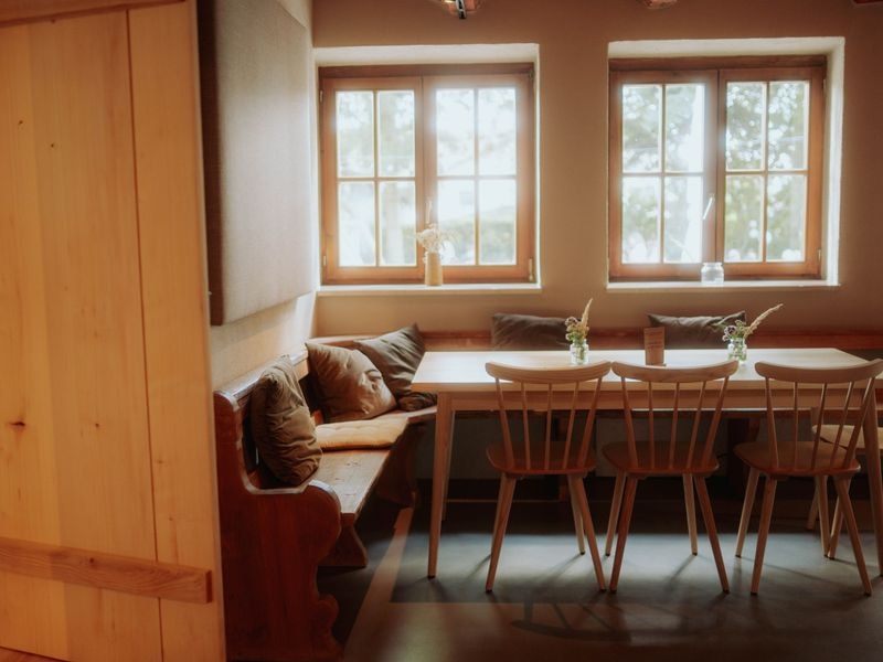 Die Stube mit Sitzbank, Kissen und langem Holztisch am Fenster