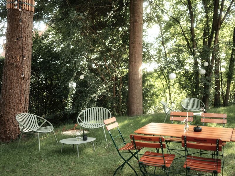 Sitzgruppe im Garten unter hohen Bäumen mit Lichterketten